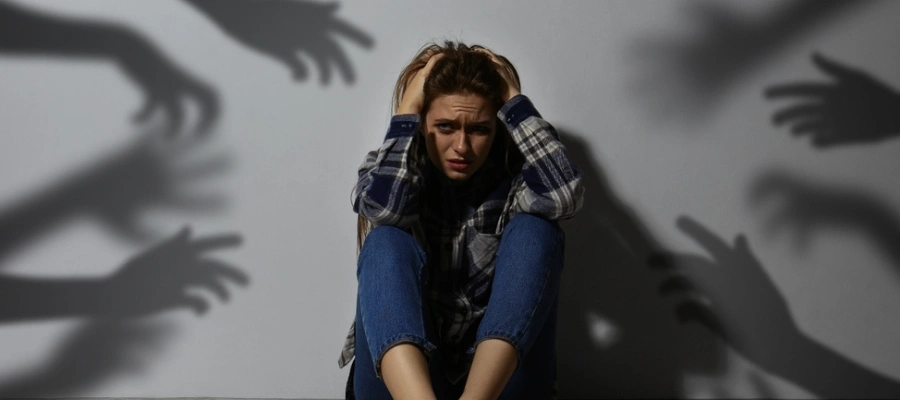 Female sitting with hands over her head with shadows of numerous hands surrounding her - Hallucinations - Most Common Symptoms of Schizophrenia