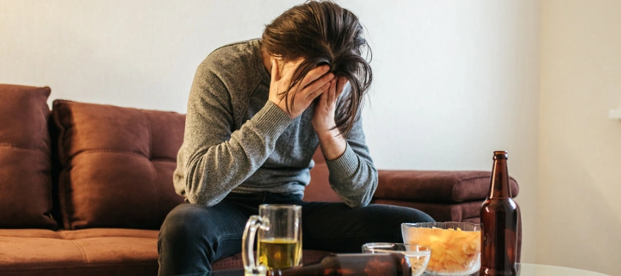 Man sitting on sofa with a beer in a mug in front of him - Why Alcohol Addiction is So Hard to Overcome Alone