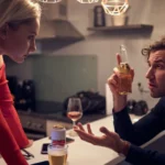Image of a woman standing with her hands on a table, looking at her husband holding a bottle of beer and expressing a bewildered look on his face - Dealing With An Alcoholic Spouse - Icarus Idaho