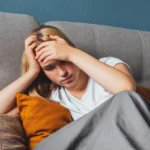 Image of a female sitting on the floor next to a sofa with her hands on her head - Do I Have Seasonal Affective Disorder Quiz - Icarus Wellness