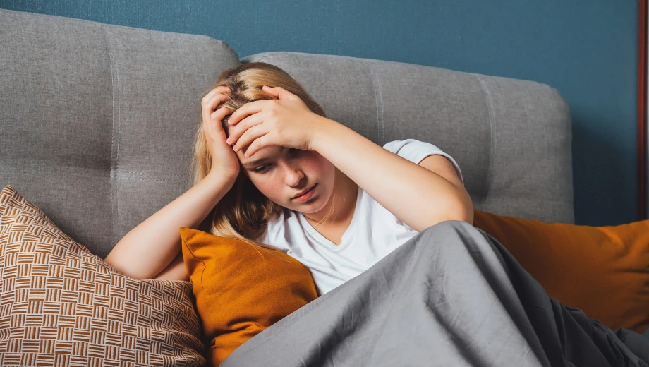 Image of a female sitting on the floor next to a sofa with her hands on her head - Do I Have Seasonal Affective Disorder Quiz - Icarus Wellness