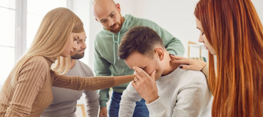Image of men and women in group therapy, gathered around man holding his hand on his face - Group therapy for borderline personality disorder treatment