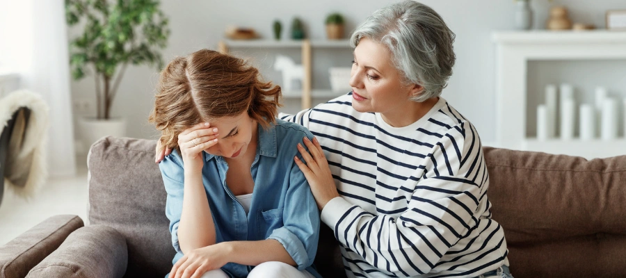 Image of an older woman consoling a younger woman in despair as both isit on a sofa -  Childhood Trauma Support