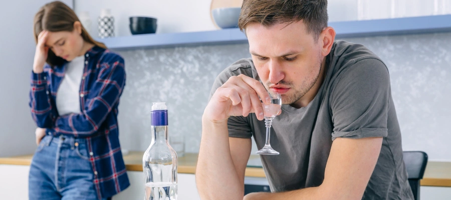 Image of an unhappy woman standing in disbelief watching husband drink, highlighting challenges of helping a high-functioning alcoholic