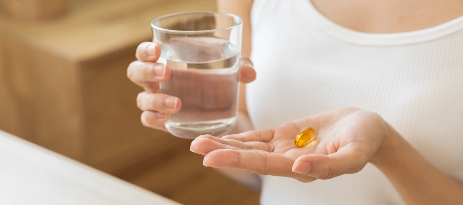 Image of a Woman holding a Vitamin D capsule in one hand and a glass of water in the other