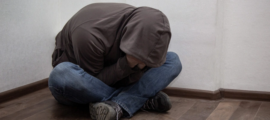 Image of person struggling with alcohol withdrawal, sitting on the floor with his head on his kneeds, highlighting the dangers of quitting cold turkey