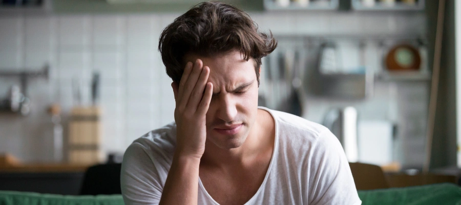 Image of a man in pain with his eyes closed and hand on his head, experiencing alcohol withdrawal symptoms