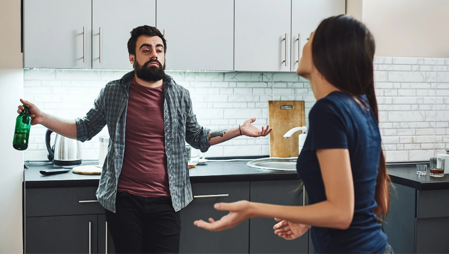 Image of a man holding a bottle of liquor in one hand having an unhappy conversation with with a woman beside him -Why an Alcoholic Cannot Love - Icarus Wellness