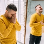 Image of a man and his reflecton in a mirror, displaying two very different emotions: somberness and happiness - Can BPD Cause Hallucinations and Psychosis - Icarus Wellness and Recovery