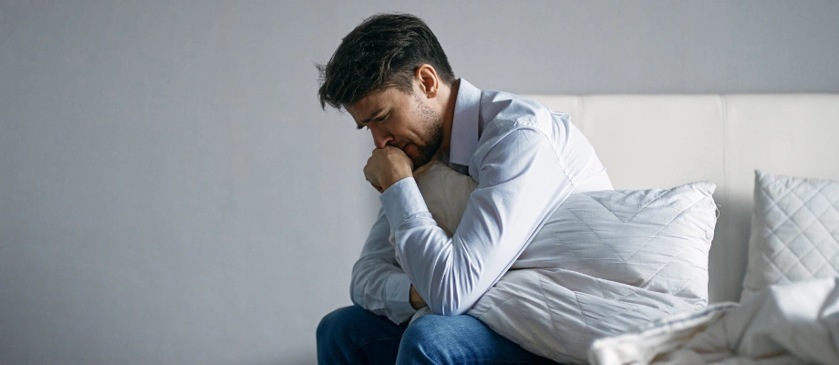 Image of a man in anguish and pain, sitting on a sofa with a pillow on his stomach