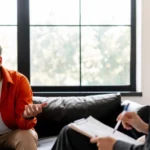 Image of a man sitting in Cognitive Processing Therapy with a female therapist - Cognitive Processing Therapy Worksheets to Support Recovery - Icarus Wellness and Recovery