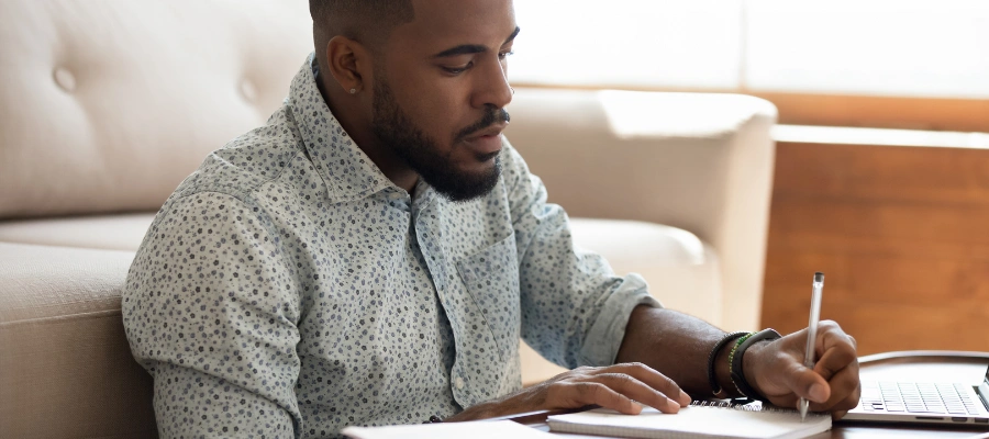 Image of a man sitting at a table, completing IFS therapy worksheets to manage his depression and build self-awareness