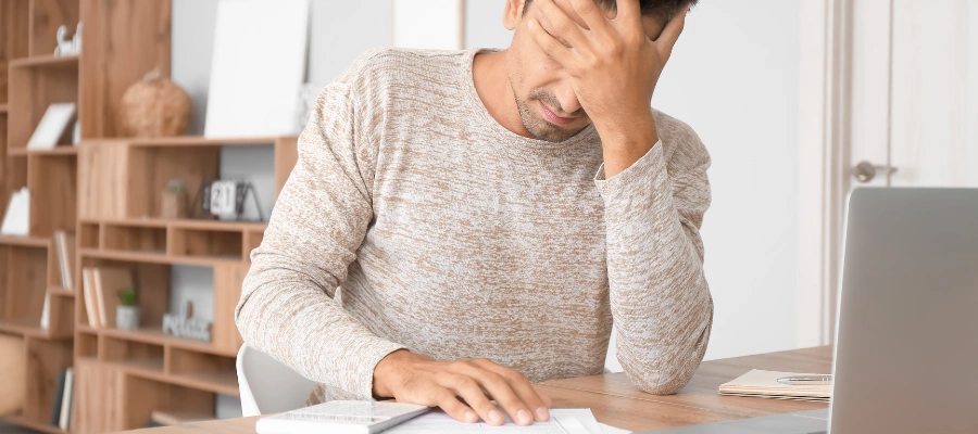 Image of a man sitting at his desk with his hand over his face, looking stressed while reviewing notes