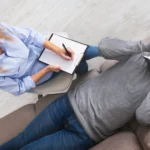 Image of a counselor talking to a male patient, lying on a sofa - REBT Therapy Worksheets and PDF - Icarus Wellness and Recovery