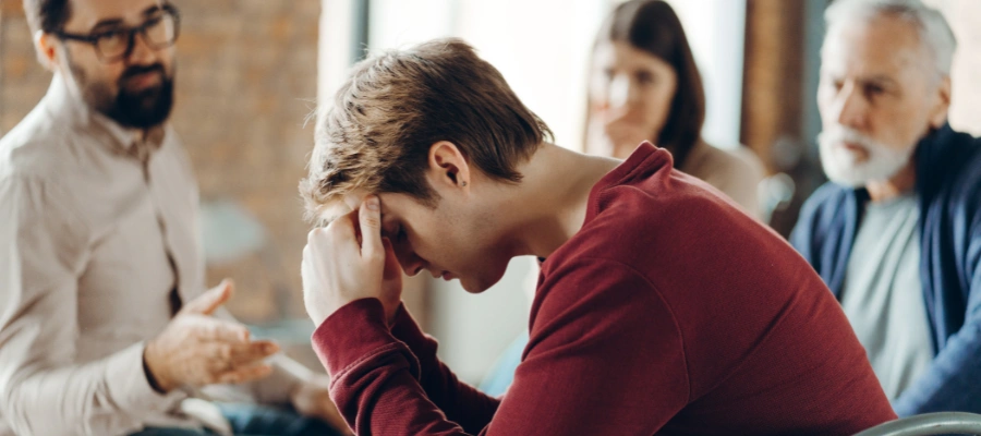 Image of of a man trying to cope with his hands on his forehead, as his family members look on