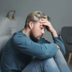Image of man sitting on the floor next to a sofa, looking confused - Why Do Addicts Relapse When Things Are Good - Icarus Wellness and Recovery Idaho