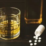 Image of a glass filled with whiskey sitting on a table next to an open vial of pills - What Are The Worst Antidepressants to Mix with Alcohol - Icarus Wellness and Recovery Idaho