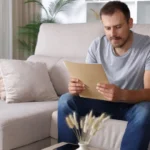 Image of a man sitting on the sofa, intently reading a document - Relapse Autopsy Worksheet and PDF - Icarus Wellness and Recovery
